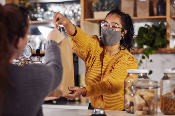 Shot of a woman wearing a mask while serving a customer in a café