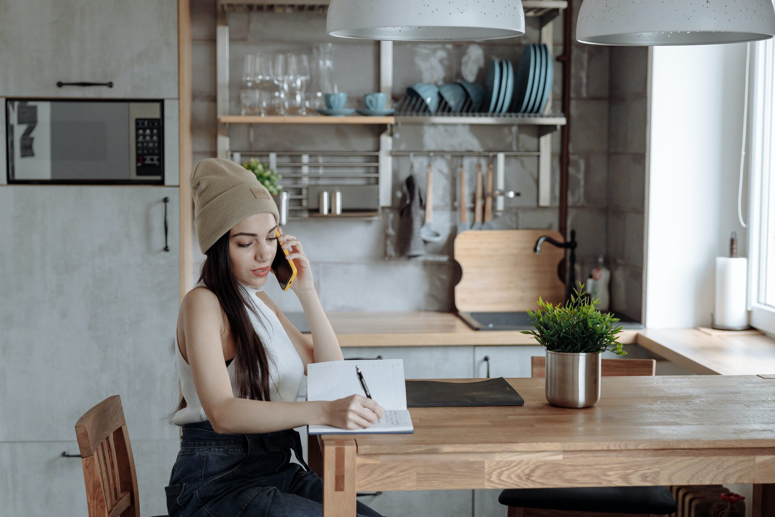 woman on the phone while taking notes in her kitchen